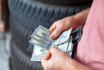 Man buying tires with dollar cash. Buying winter tyres for car to drive in cold season, man driver counting money