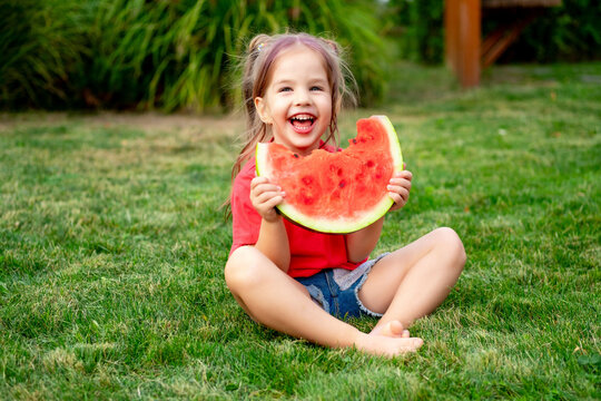 a child eats a watermelon in summer on a green lawn, a joyful little child girl eats a watermelon on the grass, a happy childhood