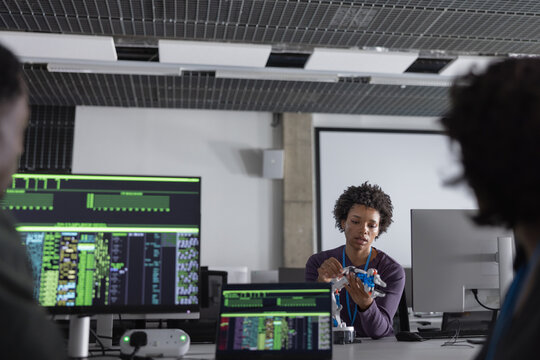 Female engineer working on a robotic arm with coding on computer monitors