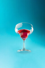 Cocktail glass in the air with blue background. Red drink in an elegant glass.