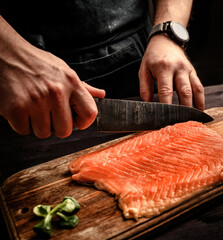 Chief cooking salmon for dinner, cutting red fish