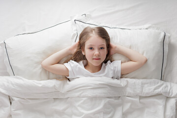 morning concept - cute little girl lying in bed under blanket