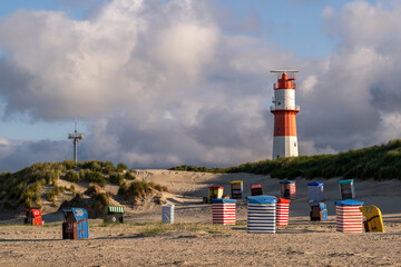 Germany, Lower Saxony, Ostfriesland, Island of Borkum with an electric lighthouse and colorful beach chairs on sandy dunes.