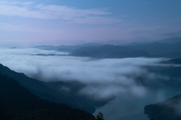 A breathtaking panoramic view of a sea of clouds below a crescent moon and a starry night sky. The silhouette of distant mountains adds depth and drama to this serene landscape. Xindian, Taiwan.