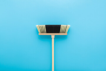 New white black broom with wooden stick on light blue table background. Pastel color. Closeup. Cleaning tool. Top down view.