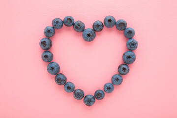 Heart shape created from fresh blueberries on light pink table background. Pastel color. Love healthy food. Closeup. Top down view.