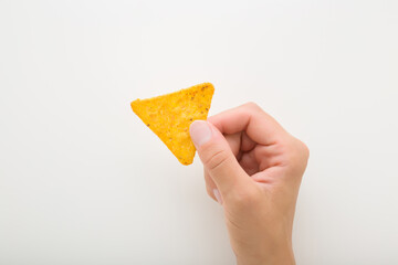 Young adult woman hand fingers holding and showing yellow tortilla chips on light gray background....