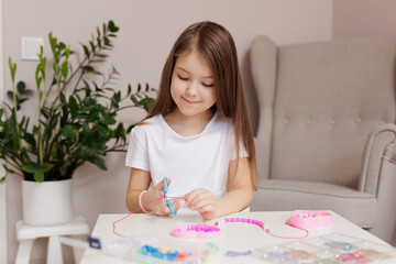 Girl making beaded jewelry at table in her room