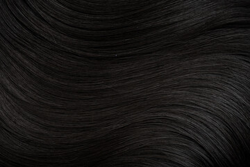 Brunette or black hair. Female long dark hair in black. Beautifully laid curls. Closeup texture in a dark key. Hairdressing, hair care and coloring. Shading gray hair. Background with copy space.