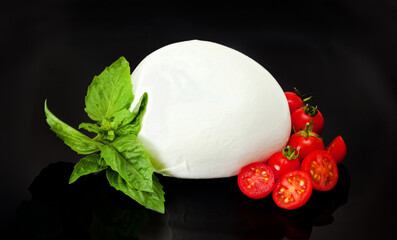 Fresh mozzarella cheese with tomato and basil on black background
