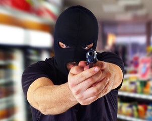 Masked criminal pointing gun in grocery store