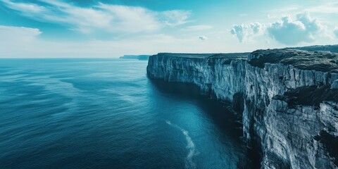 A serene coastal landscape showcasing rugged cliffs beneath a bright blue sky and tranquil ocean waves.