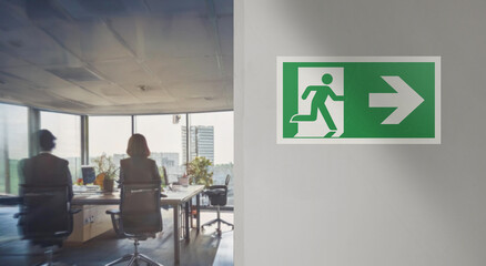 Right emergency exit sign installed on the wall of a modern office blurred in the background. Space for text insertion. Image with warm tones and colors.