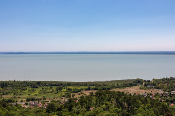 Obraz premium Panoramic aerial view of Balaton lake seen from observation tower Padkui Kilato in Balatongyorok, Hungary, Europe. Small villages along the lakeshore surrounded by rolling hills and lush greenery