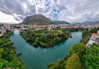 Aerial view of Old Bridge of medieval town Mostar spanning the Neretva River, Bosnia and Herzegovina. UNESCO World Heritage Site. Ancient arch stone structure on cloudy day surrounded by minarets