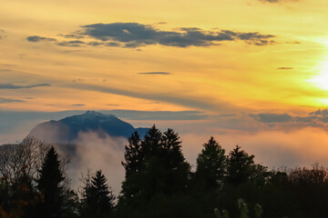 Fiery sunset over mountain summit Dobratsch in Rosental, Carinthia, Austria, Europe. Silhouette of forest and rolling hills in Austrian Alps. Vibrant orange and yellow hues. Tranquil serene atmosphere