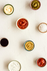 Set of bowls with sauces pesto salsa mustard and others, top view. Food background