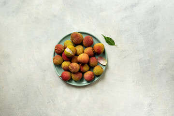 Juicy fresh lychee fruit with cut in half and green leaves on the plate, top view