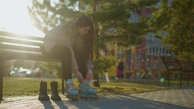 A person sitting on a bench in a park, loosening the straps of one rollerblade while wearing another. The scene captures a quiet moment of transitioning from skating to regular footwear