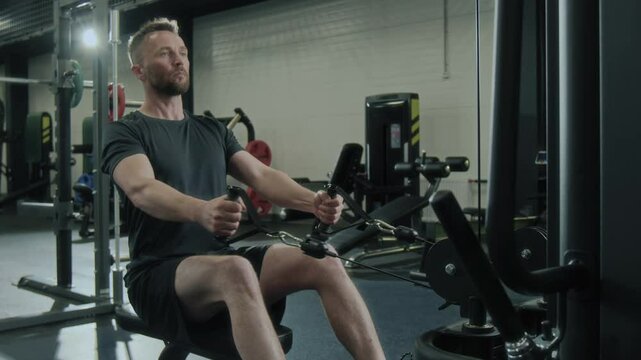 Athletic man in sportswear using rowing machine for workout in gym during strength training session