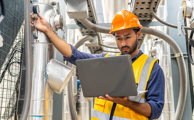 Male technical foreman in safety uniform inspects maintenance work work holding a laptop to look at...