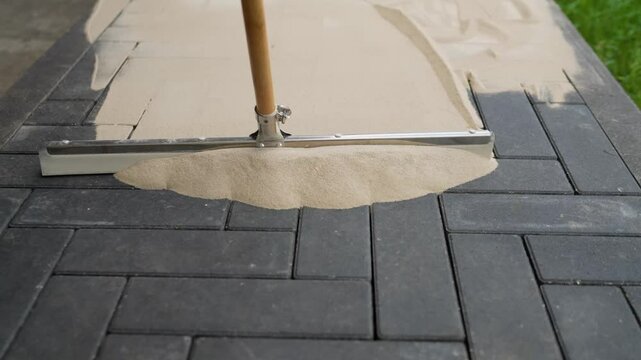 A worker with a grouting brush and spot tiles, pavement laying industry. A worker fills cracks between tiles with sand. Seals joints between tiles. A worker rubs sand between tiles. A worker fills cra