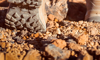 Legs in hiking boots closeup, a girl walks on a rocky desert terrain.
