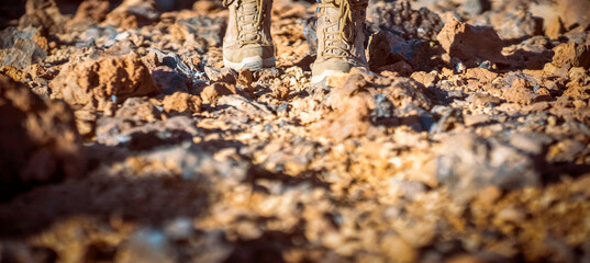Legs in hiking boots closeup, a girl walks on a rocky desert terrain.
