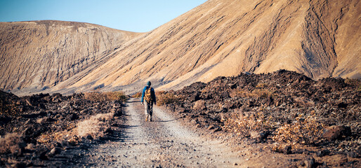 A man is traveling, hiking among mountains and volcanoes in the desert with a backpack.