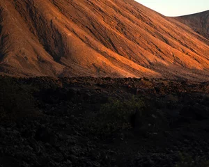 Fototapeten A volcanic landscape with black lava formations and a mountain in the sun. © Zhanna