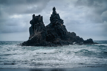 A dark rocks amist stromy wavy ocean in a cloudy weather.