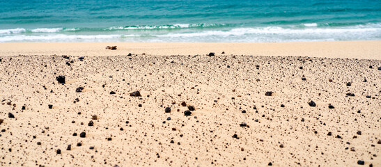 A sandy beach on the coastline of the ocean with clear blue water.