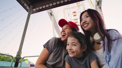 A lesbian family joyfully chats and points at various landmarks from the Ferris wheel. Excited and engaged, they share a fun moment, exploring the city from high above together