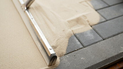 A worker fills cracks between tiles with sand. Seals joints between tiles. A worker rubs sand...