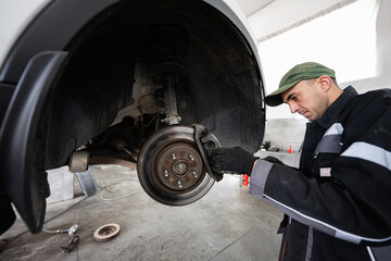 A focused mechanic carefully inspects the brake system of a vehicle in a professional auto repair shop. Expertise and attention to detail are emphasized in this automotive maintenance scene.