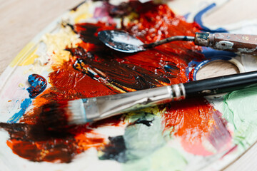 Fototapeta premium Artists palette filled with vibrant colors and brushes on a wooden surface