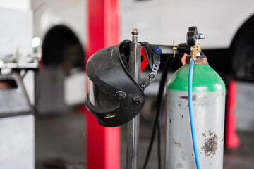 Close-up of a welding helmet and gas cylinder in an automotive workshop, representing industrial safety and tools in a modern work environment.