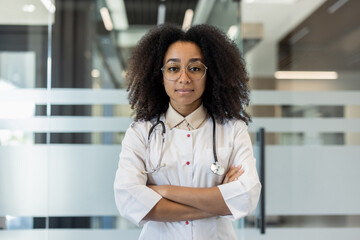 Close-up portrait of a young serious African-American woman wearing glasses and a white coat,...