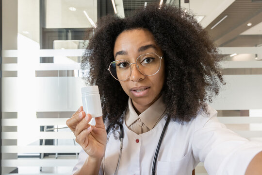 Close-up photo of a young African female doctor pharmacist in a hospital, talking and showing a jar of pills to the camera