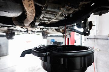 A detailed view of an oil change taking place in an automotive repair garage. Oil is draining from...