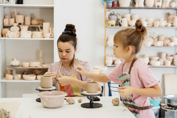 Two children shaping clay pottery in a bright art studio with various supplies