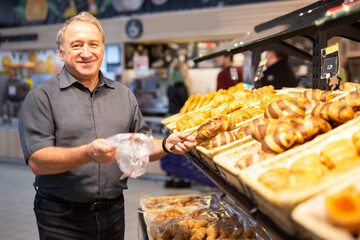 Man takes muffins on shelf of bakery section