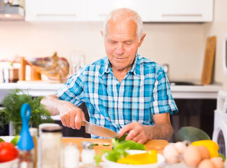 Senor man preparing fresh vegetable salad at home in the kitchen