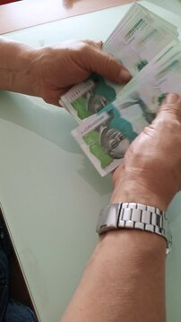An unrecognizable man counts 100,000 Colombian peso bills on a glass table. Colombian money.