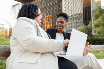 Two African American women discussing work outdoors with a laptop