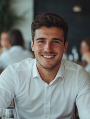 Fototapeta premium Handsome young man smiling at the camera, sitting in a modern restaurant with blurred background of other patrons.