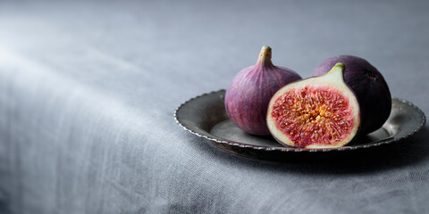 Fresh figs on a dark background, whole and a piece, ripe, delicious and sweet seasonal dessert with a rustic plate on a dark tablecloth