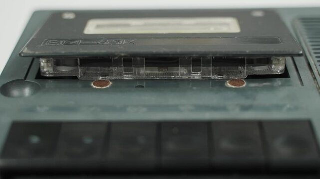 Old cassette recorder. Hand presses eject button on vintage boombox, revealing a cassette tape inside. This close-up shot captures the simple action of removing media from a classic music player.