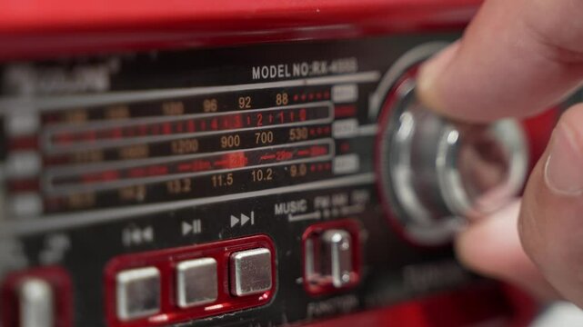 Close-up shot of boombox radio dial. Hand turns tuning knob, adjusting the orange indicator as it scans various radio frequencies, searching channel. Tuning frequency analog radio station 