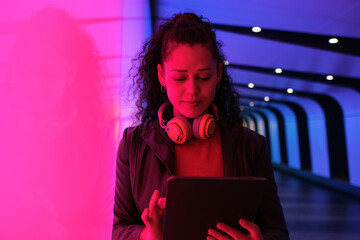 Young woman using tablet in neon tunnel at night